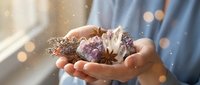 Hands holding collection of healing crystals and natural elements with magical sparkles and warm bokeh lighting for spiritual wellness practices.