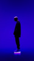 Silhouette of person in dark clothing standing against vibrant purple background, illuminated by neon light at feet, creating dramatic contrast for fashion or music concepts.