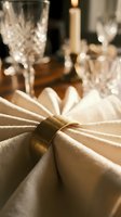 Elegant formal dining table setting with cream napkin tied with gold napkin ring, crystal glassware, and candlelit ambiance for upscale events and hospitality design.