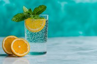 Refreshing sparkling water with orange slice, mint leaves and bubbles in glass on turquoise background. Fresh citrus fruit slices on table. Summer drink concept.
