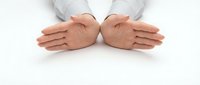Professional hands in white shirt sleeves positioned protectively over white surface, symbolizing care, security and business protection concepts.