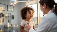 Happy mixed-race toddler girl laughing during pediatric checkup with female doctor in modern medical office. Child healthcare and wellness examination.