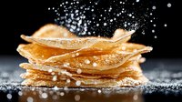 Stack of crispy thin crepes or pancakes with powdered sugar falling in motion against dark background, macro food photography for restaurant menu.