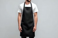 Professional male chef wearing black apron over white shirt standing against neutral background for culinary branding and restaurant marketing materials.