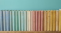 Row of vintage books with colorful spines in pastel blue, green, beige, pink and yellow tones arranged on wooden shelf for library or study decor.