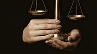 Hands holding golden scales of justice against dark background symbolizing legal system fairness and judicial balance in courtroom proceedings.