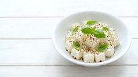 Fresh tofu cubes with sesame seeds and green herbs in white bowl on wooden background for healthy Asian cuisine and vegetarian cooking concepts.