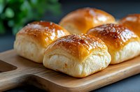 Fresh homemade dinner rolls with glossy golden brown tops served on wooden cutting board, soft fluffy texture and buttery shine against dark background.