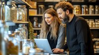 Young couple shopping together in modern zero waste bulk store browsing laptop for sustainable products and eco-friendly lifestyle choices.