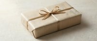 Elegant kraft paper gift box with golden satin ribbon bow on neutral background for special occasions and celebrations.