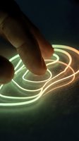 Finger touching glowing neon sneaker sole with green and orange light trails on dark background, representing futuristic footwear technology and innovation.