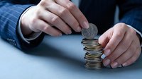 Businessman in suit stacking coins with hands protecting money tower representing financial growth, savings strategy and investment planning.