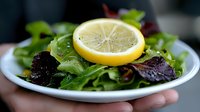 Fresh mixed green salad with arugula, purple basil leaves and bright lemon slice on white plate, selective focus. Healthy Mediterranean cuisine.