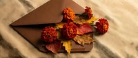 Autumn envelope with orange marigold flowers and colorful fall leaves on rustic linen fabric, warm seasonal flat lay for greeting card design.