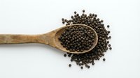 Wooden spoon filled with black peppercorns scattered on white background. Organic spice ingredient for cooking and seasoning isolated for culinary design.