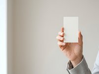 Person with medium skin tone holding blank white card or paper in hand against neutral background. Suitable for business, marketing, advertising, and promotional campaigns.