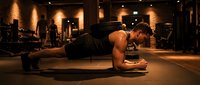 Athletic Caucasian man performing plank exercise on yoga mat in modern gym with warm lighting. Fitness training workout for core strength and endurance.