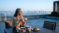 Elegant businesswoman enjoying morning coffee on luxury rooftop terrace with city skyline view during golden hour sunrise for lifestyle content.