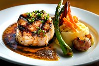 Grilled pork medallion with rich brown sauce, served alongside mashed potatoes, sauteed asparagus, and glazed baby carrots on white plate, fine dining presentation.