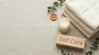 Flat lay self care concept with folded towels, lit candle, dried orange slice, eucalyptus and wooden sign on linen background.