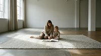 Young Caucasian mother and toddler son sitting together on woven rug in minimalist living room with natural light streaming through windows.