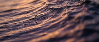 Golden sunset light reflecting on gentle ocean waves with soft ripples and warm amber tones creating peaceful seascape for relaxation and meditation backgrounds.