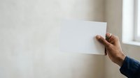 Mature male hand holding blank white card against neutral wall background, suitable for mockups and promotional designs.