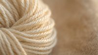 Soft cream colored yarn ball with twisted fibers in warm natural lighting, perfect for knitting and crochet projects, crafting supplies and textile work.