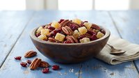Wooden bowl filled with mixed nuts and dried cranberries on rustic blue table, healthy snacking and cooking ingredients for recipes.