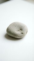 Single smooth gray pebble stone with natural holes on clean white surface for zen meditation spa wellness and minimalist design concepts.
