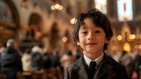 Young Asian boy in formal suit and tie smiling warmly inside church with soft bokeh lights and blurred crowd in background, capturing innocence and spirituality.