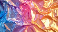 Vibrant metallic foil texture in pink, blue and gold colors creates abstract wrinkled surface with dynamic light reflections and shimmering iridescent effect.