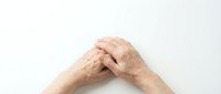 Elderly hands clasped together in prayer or meditation pose against clean white background showing wrinkles and age spots on mature skin.