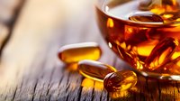 Amber-colored omega-3 fish oil supplements in soft gel capsules on rustic wooden surface with warm backlighting creating golden glow and reflections.