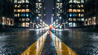 Urban night street scene with wet asphalt reflecting colorful city lights and illuminated office buildings creating atmospheric bokeh effect for modern lifestyle concepts.