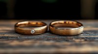Wedding rings on rustic wooden surface with one ring featuring small diamond accent, romantic close-up shot showing brushed metal texture and warm golden tones.