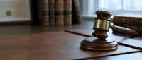 Wooden gavel with brass band on sound block in courtroom setting with law books, symbolizing justice, legal proceedings, and judicial authority.