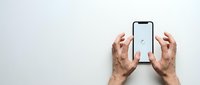 Hands holding modern smartphone with blank white screen on clean white background, perfect for app mockup presentations and digital marketing materials.