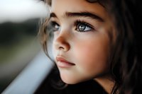 Close up portrait of young girl with striking blue eyes and natural makeup looking thoughtfully through window, soft natural lighting creates dreamy atmosphere.