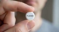 Hand holding white placebo pill tablet for medical research study clinical trial pharmaceutical testing concept.