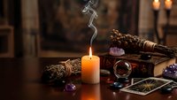 Mystical altar setup with burning candle, sage bundles, crystals, tarot cards and ritual tools for spiritual practices and meditation ceremonies.