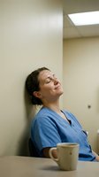 Exhausted female healthcare worker in blue scrubs taking coffee break, leaning against hospital wall with eyes closed, showing medical professional fatigue.