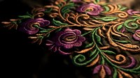 Intricate floral embroidery with purple roses and golden threads on dark fabric showcasing traditional needlework craftsmanship and decorative textile art.