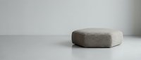 Minimalist hexagonal upholstered ottoman in soft beige fabric on a neutral gray floor against a light wall in a modern interior.