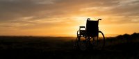 Silhouette of empty wheelchair against golden sunset sky over rural landscape, symbolizing hope, recovery, and resilience for healthcare and wellness content.