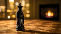 Black chess king piece standing on wooden surface with warm fireplace bokeh lights creating cozy indoor atmosphere for strategic game concepts.