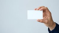 Close-up of male hand holding blank white business card against neutral background for corporate branding and marketing purposes.