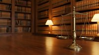 Golden scales of justice on wooden desk in traditional law library with leather-bound books and warm lighting for legal consultation and attorney services.