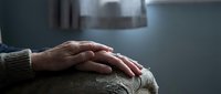 Adult hand with manicured nails resting gently on elderly person's arm, showing compassion and care in healthcare or family support setting.