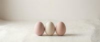 Three fresh chicken eggs arranged in row on neutral beige textured surface with soft natural lighting for cooking and food photography concepts.